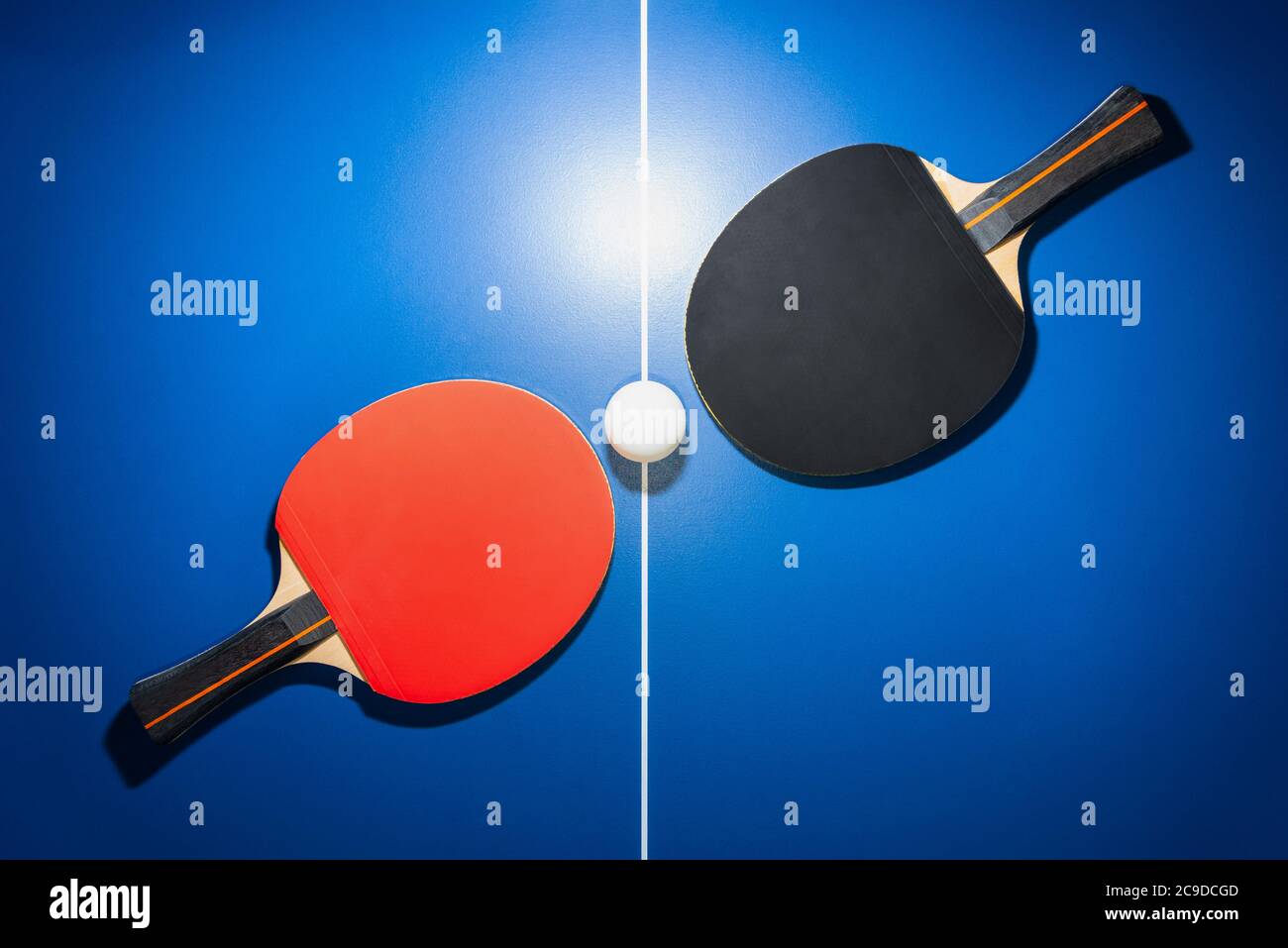 Vue de dessus une raquette de ping-pong noir et rouge et une balle de ping-pong blanche sur la table de ping-pong bleue avec un spot lumineux, deux paddle de ping-pong est Banque D'Images