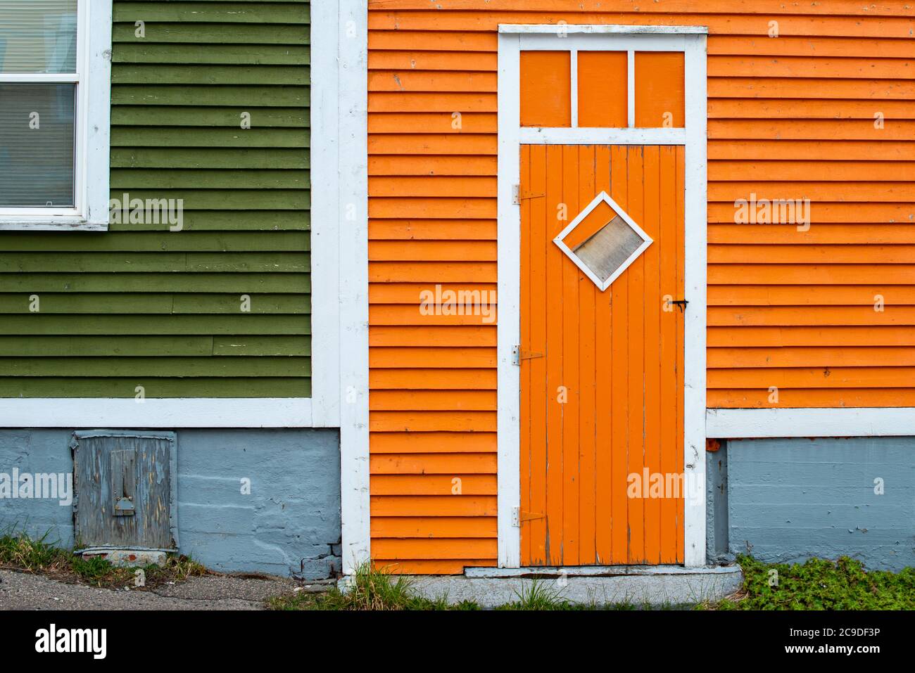 Une porte extérieure en bois orange avec une fenêtre en forme de losange dans un bâtiment à panneaux de bois orange et vert. Banque D'Images