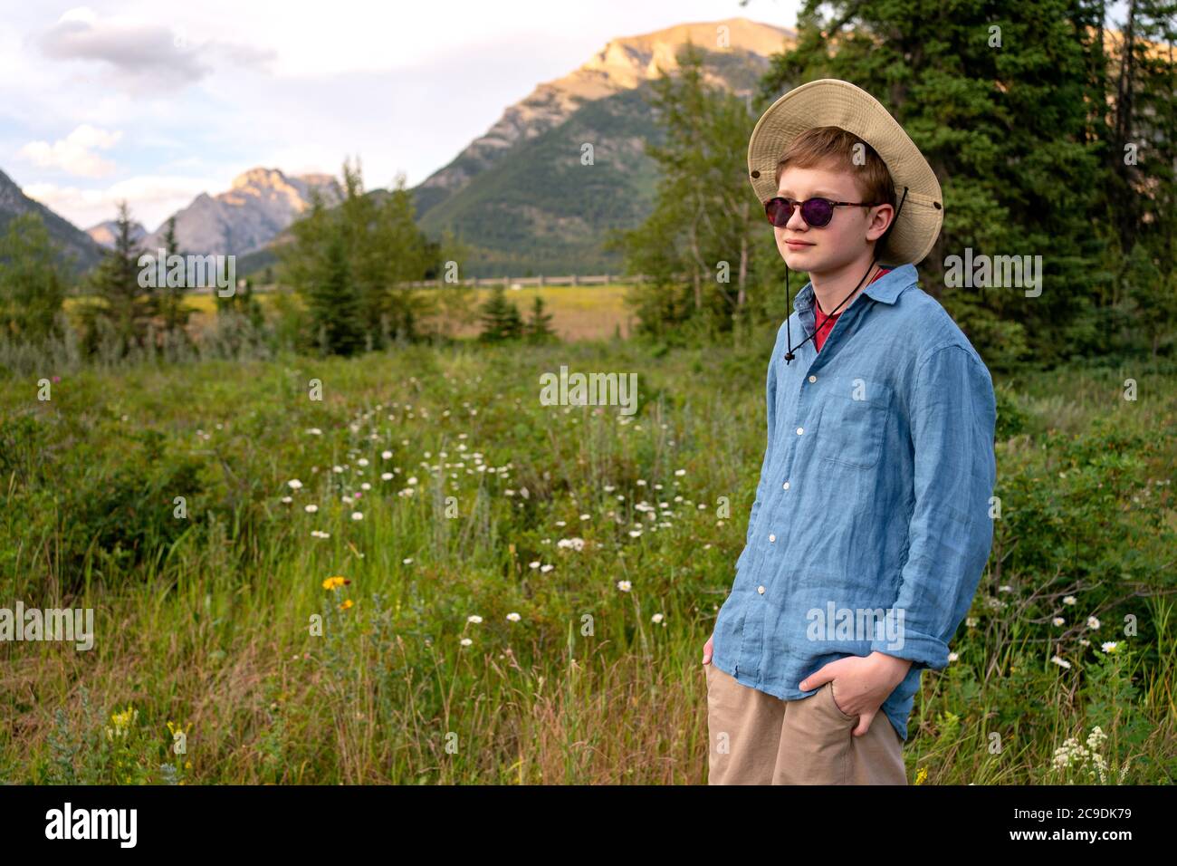 Adolescent voyageur portant un chapeau et des lunettes de soleil, restant détendu à l'extérieur avec des montagnes rocheuses sur le fond. Concept de vacances d'été. Banque D'Images