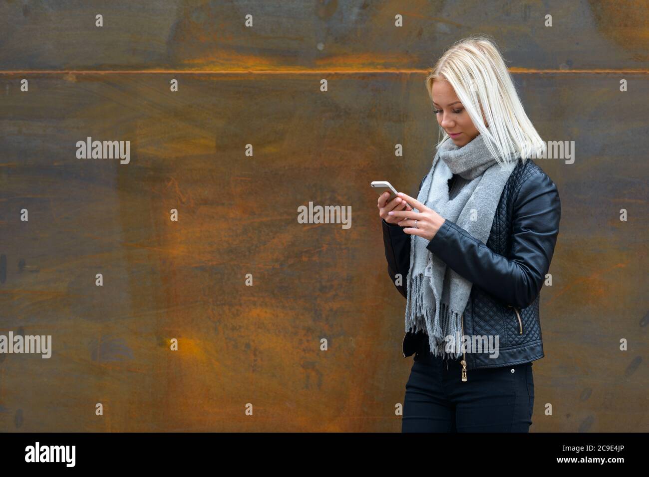Jeune belle femme blonde utilisant un téléphone mobile contre un vieux mur en métal rouillé Banque D'Images