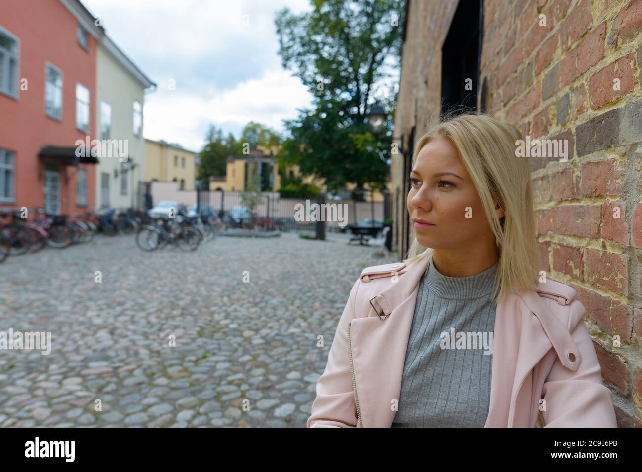 Jeune belle femme blonde penchée contre le mur de brique dans le parking de vélo Banque D'Images
