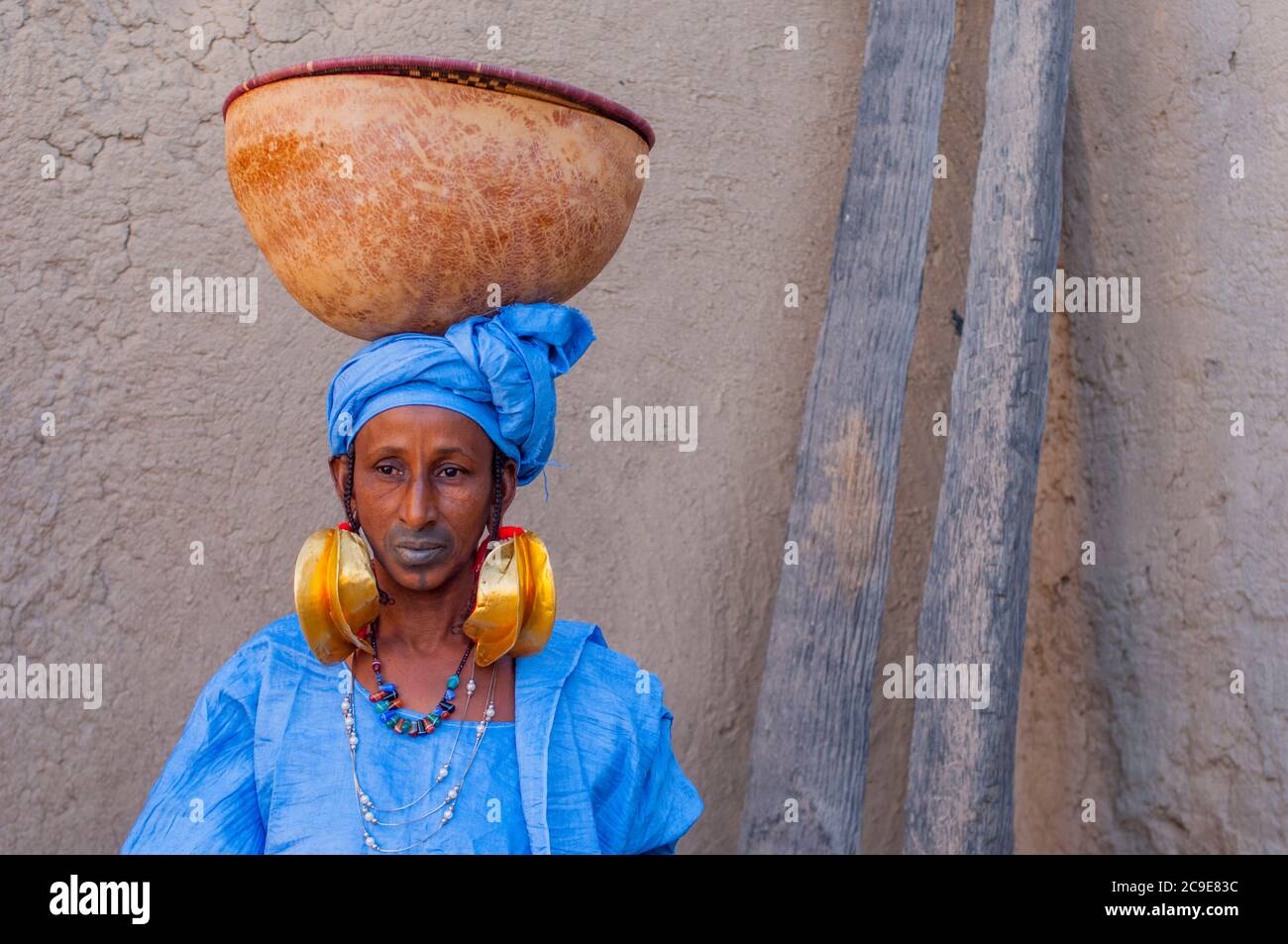 Une femme tribale de Fulani avec boucles d'oreilles en or festives et lèvres tatouées portant un calabash à Mopti au Mali, en Afrique de l'Ouest. Banque D'Images