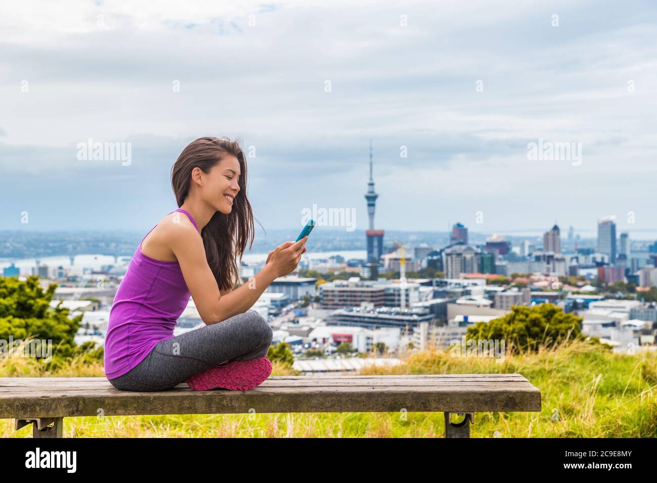 Une jeune fille de la ville d'Auckland qui utilise l'application pour  téléphone portable dans le parc d'été Skyline. Vue sur le paysage urbain  depuis le mont Eden, dans l'île du Nord, en