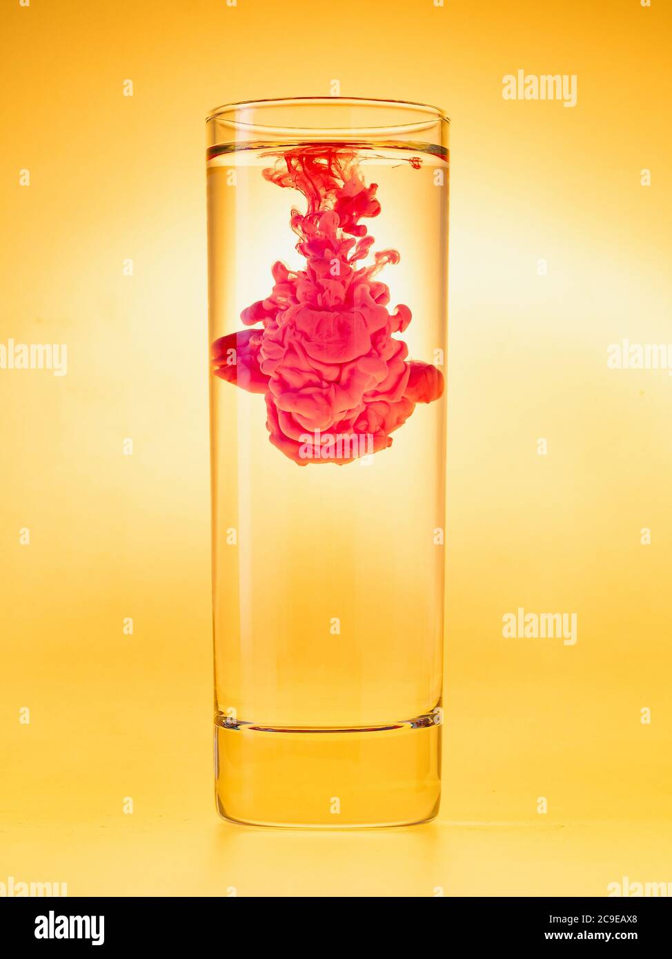 Nuage d'encre dans un verre d'eau. Peinture rouge dans l'eau sur fond jaune. Combinaison de couleurs analogique. Prise de vue en studio. Banque D'Images