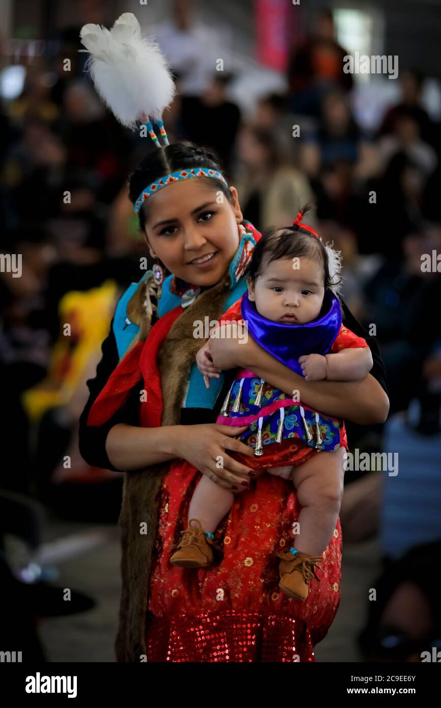 San Francisco, États-Unis - 08 février 2020 : jeune femme amérindienne ou indienne vêtue d'une tenue traditionnelle colorée tenant une petite fille sous le coup d'un pow-wow Banque D'Images