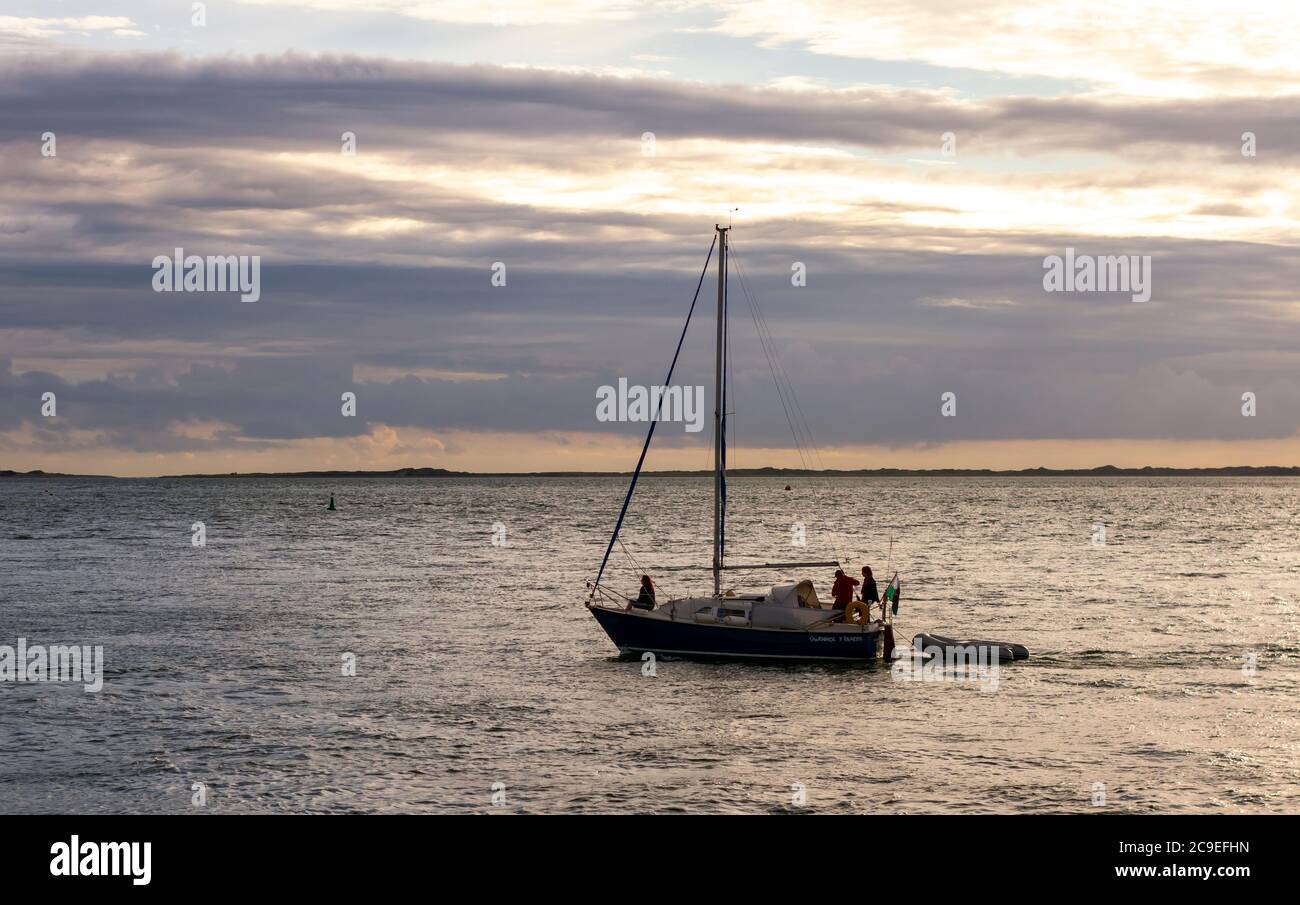 Anglesey, pays de Galles, Royaume-Uni 08/26/2012: Un petit bateau avec trois passagers navigue au large de la côte du pays de Galles au coucher du soleil. Un bateau gonflable est attaché à TH Banque D'Images