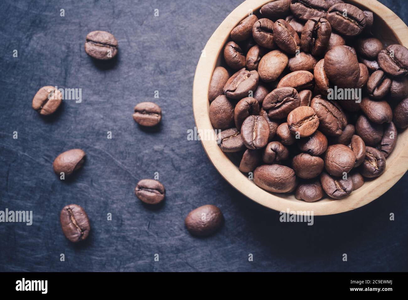 gros plan d'un bol en bois rempli de grains de café rôtis sur fond d'ardoise foncé. format horizontal avec espace de copie pour le texte. vue directement au-dessus Banque D'Images