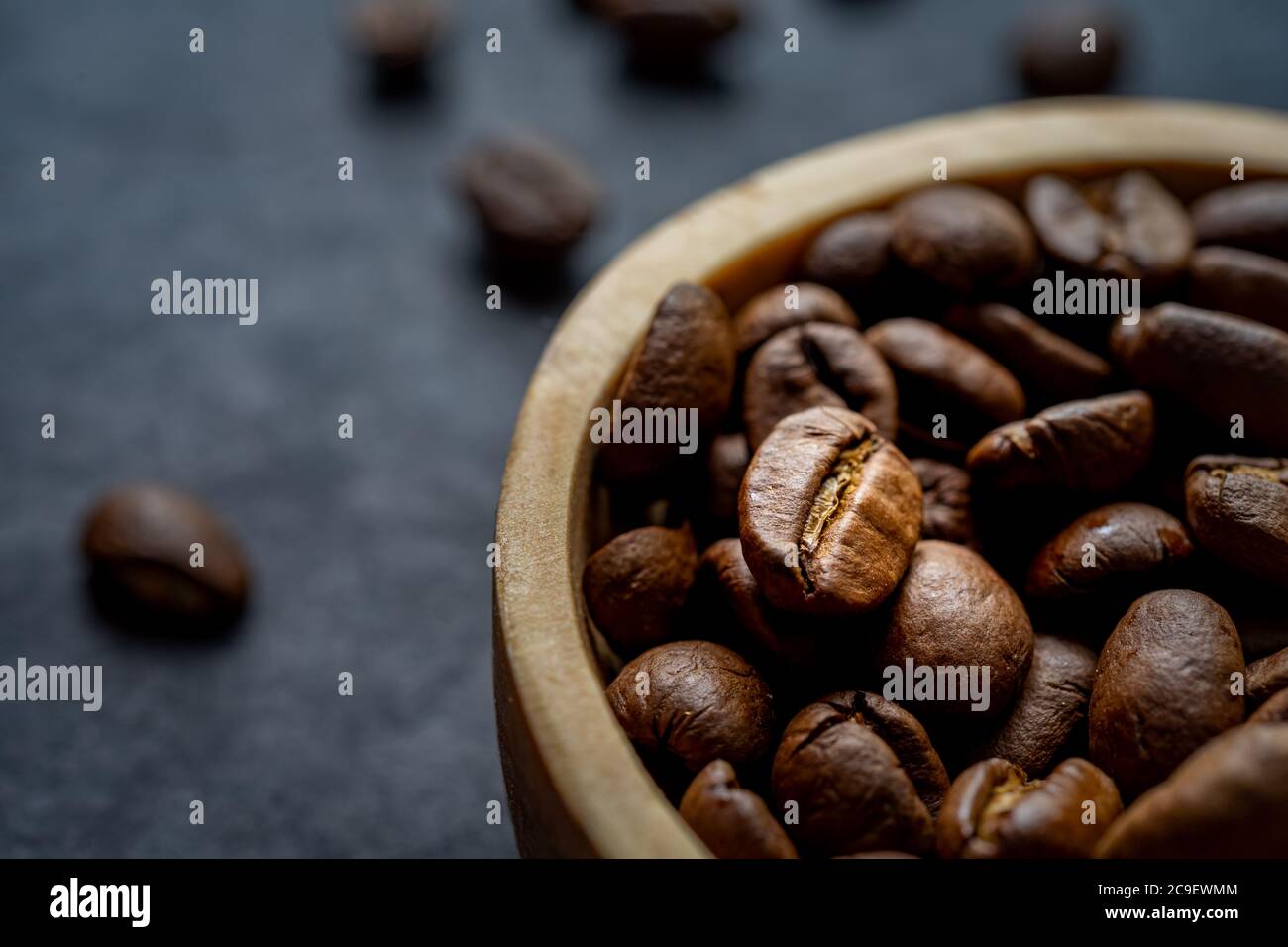 gros plan extrême d'un bol en bois rempli de grains de café rôtis sur fond d'ardoise foncé. format horizontal avec espace de copie pour le texte Banque D'Images