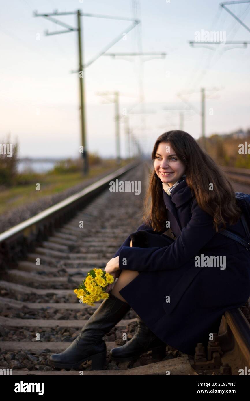 Une fille marche sur des rails de chemin de fer dans un manteau avec des fleurs - voyage, dépression, style de vie, amour Banque D'Images