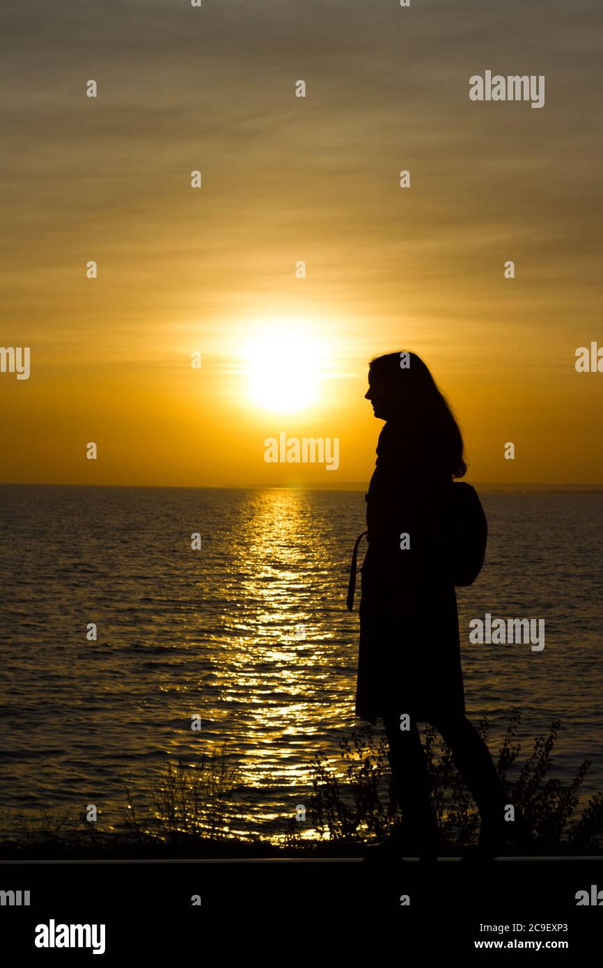 Une fille marche sur des voies de chemin de fer dans un manteau et des bottes sur un fond de coucher de soleil - voyage, dépression, style de vie Banque D'Images