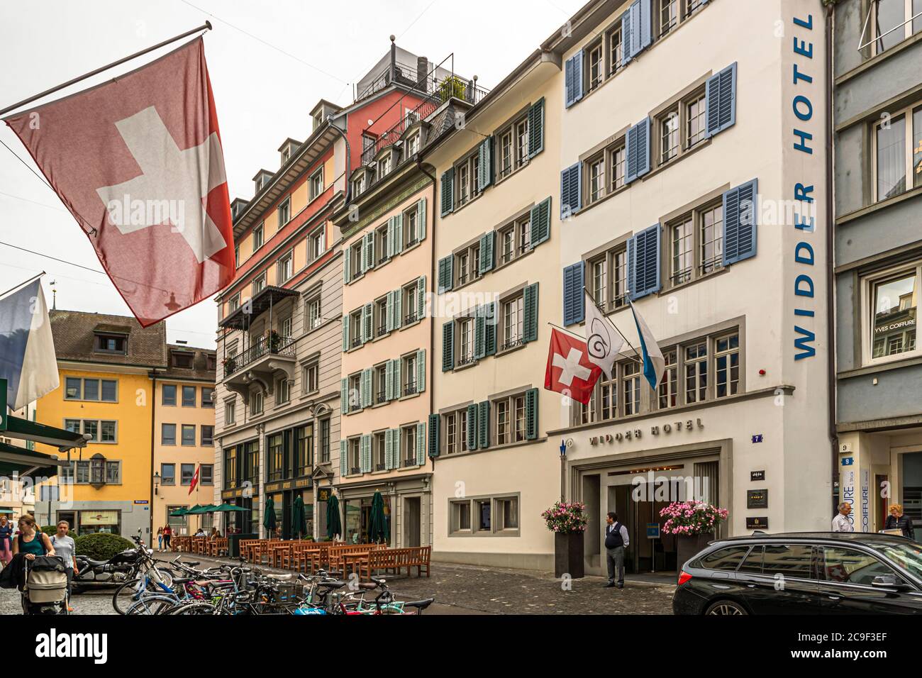 Le drapeau suisse flotte devant la façade de l’hôtel Widder sur la Renngasse à Zurich, en Suisse. Derrière l’ancienne façade se cache un cœur luxueux : ce qui ressemble de l’extérieur à une rangée de bâtiments anciens voisins est en fait une structure ultra-moderne. Huit bâtiments classés, autrefois maison de la guilde Zunft zum Widder, établie ici en 1401, ont été combinés en hôtel en 1995 après une rénovation de dix ans dirigée par l’architecte Tilla Theus. Banque D'Images