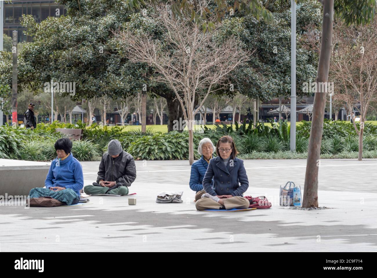 Un matin hivernal à Darling Harbour, Sydney, Australie, un petit groupe de personnes asiatiques plus âgées s'assoient en croix sur le sol et méditent Banque D'Images
