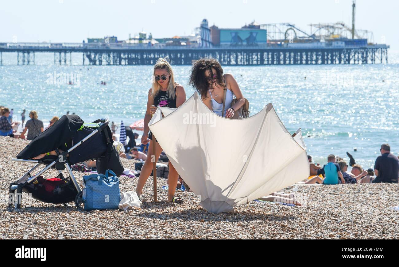 Brighton Royaume-Uni 31 juillet 2020 - il est temps de monter le parapluie pour obtenir un peu d'ombre alors que les foules affluent aujourd'hui à Brighton Beach sur ce qui devrait être le jour le plus chaud de l'année jusqu'à présent avec des températures qui devraient atteindre plus de 30 degrés dans le sud-est . Le temps est alors réglé pour se rafraîchir au cours du week-end: Crédit Simon Dack / Alamy Live News Banque D'Images