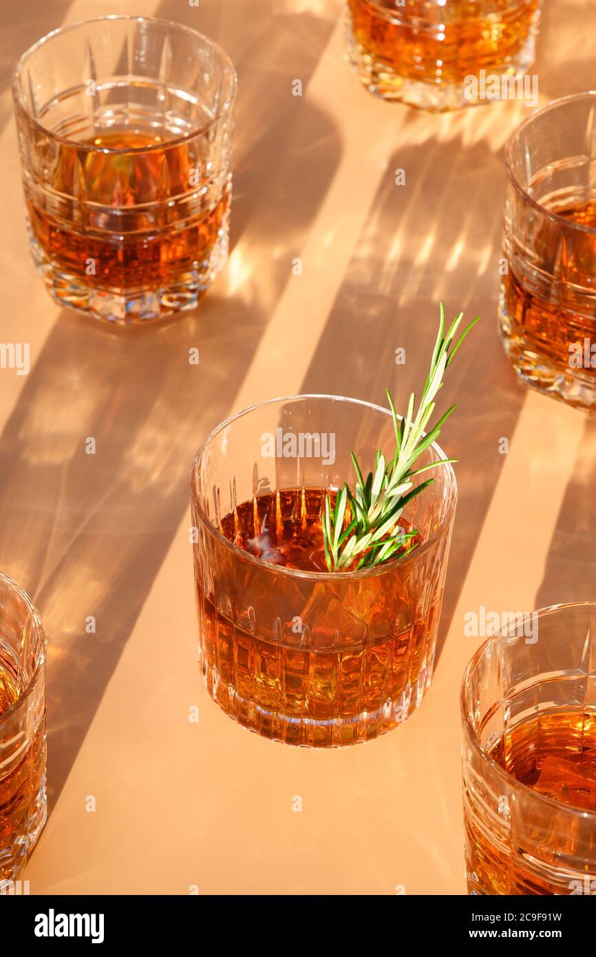 De nombreux verres de whisky froid servis dans des rochers au romarin sur fond beige tendance. Format vertical. Banque D'Images