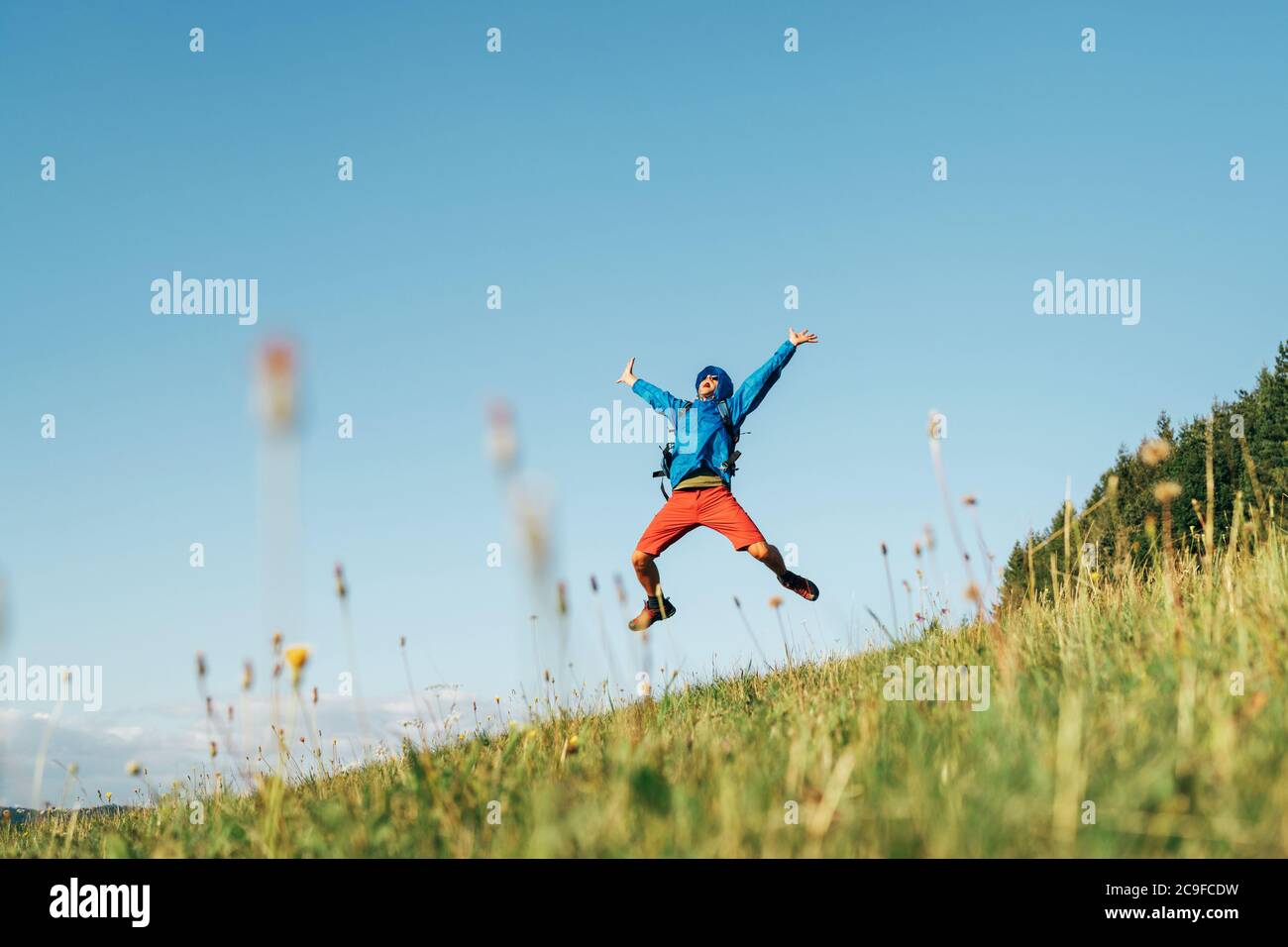 Backpacker voyageur saut émotionnellement sur l'herbe verte montagne prairie avec sac à dos avec les bras et les jambes ouverts larges. La liberté de l'homme dans la nature conce Banque D'Images