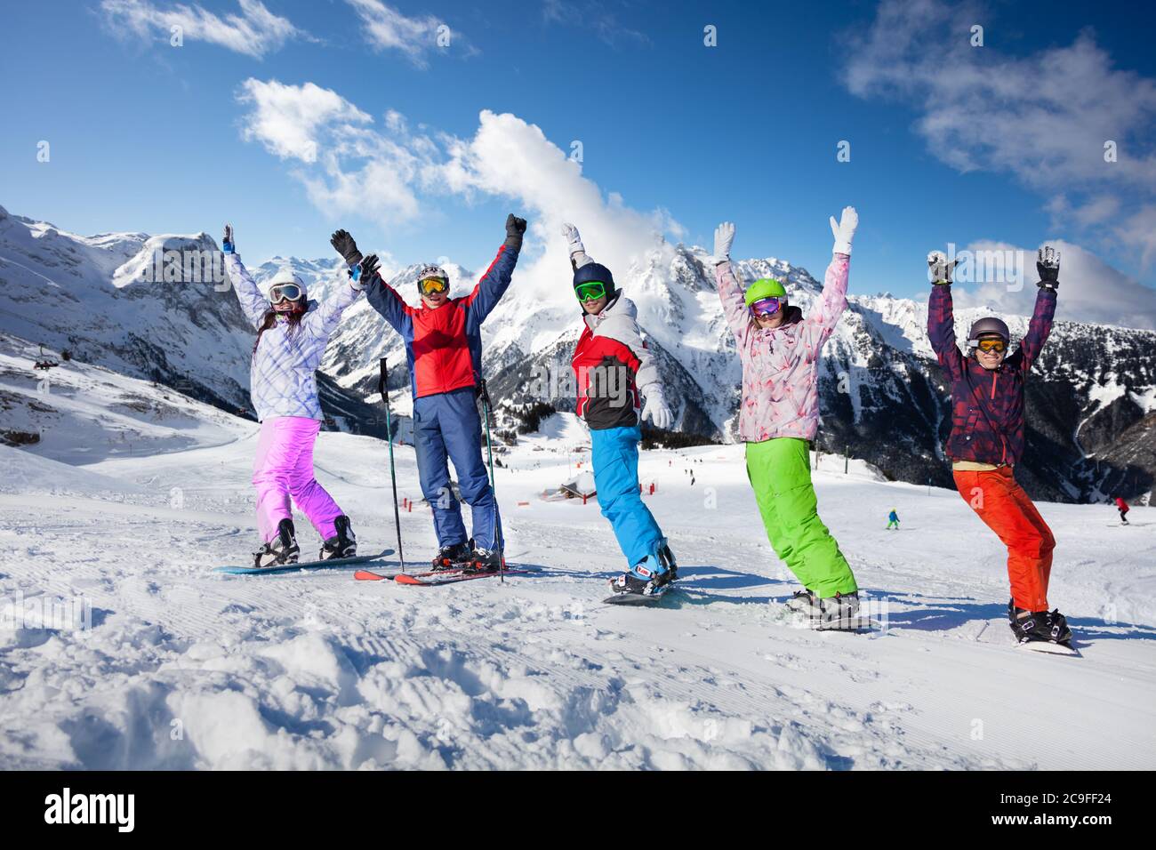 Groupe de jeunes adultes sur le ski et les planches de neige se tiennent ensemble dans la rangée en levant les mains au-dessus des sommets de montagne Banque D'Images