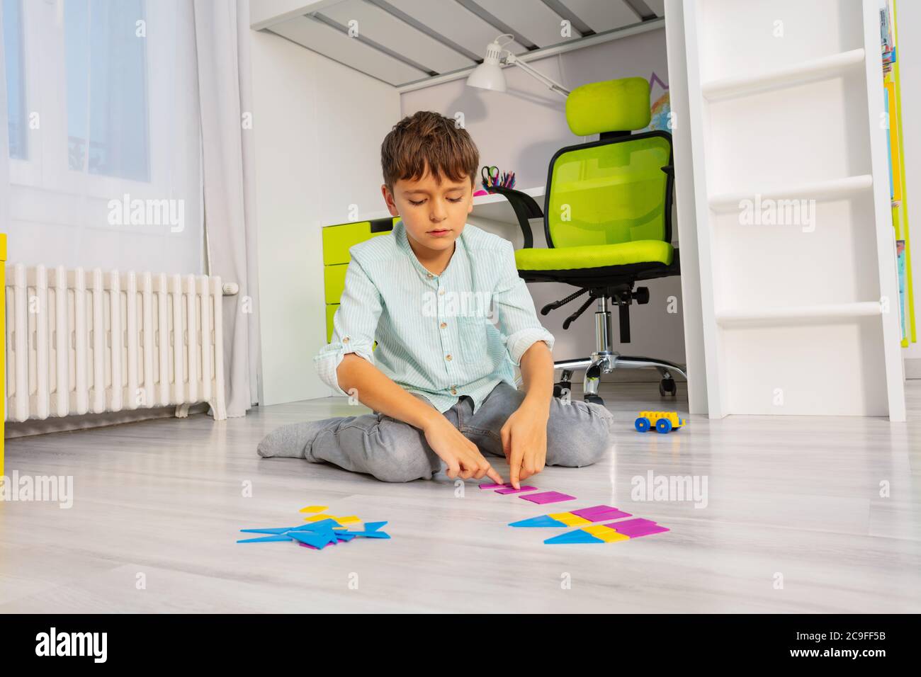 Un garçon calme a mis des formes géométriques dans l'ordre assis sur le sol dans la chambre des enfants Banque D'Images