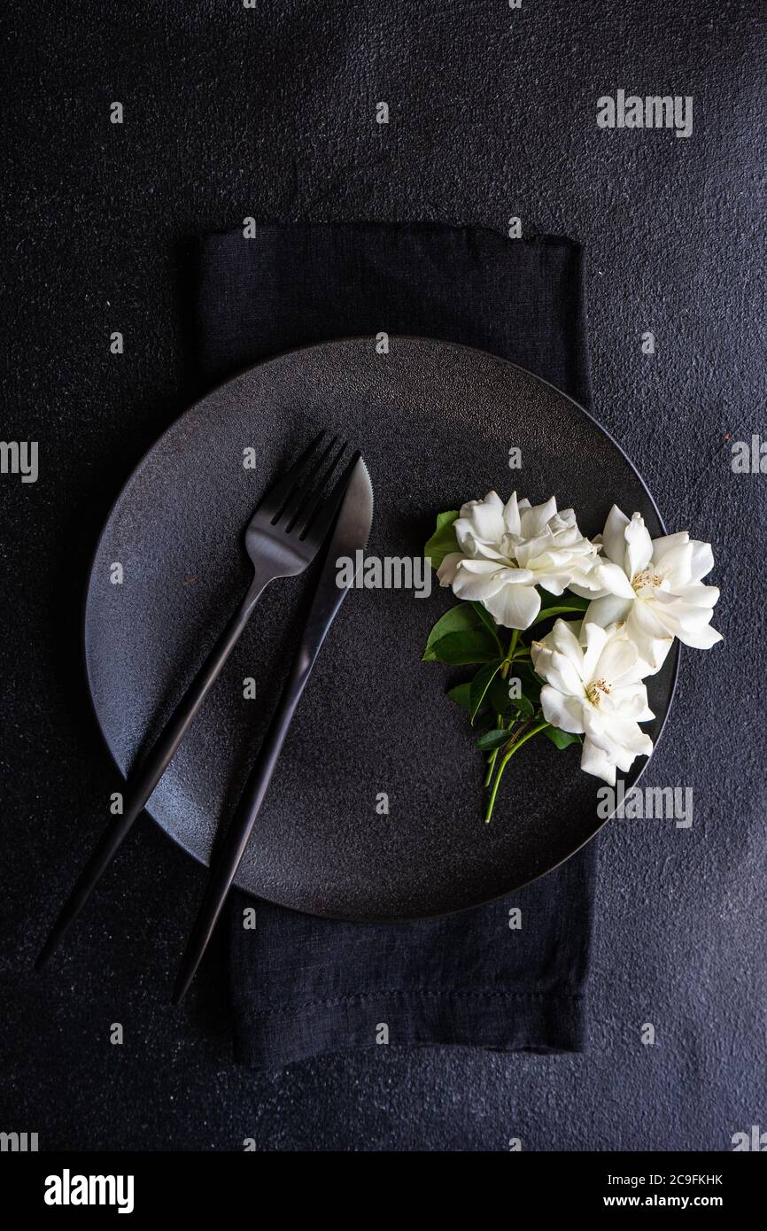 Table minimaliste en grès noir et couverts décorés de fleurs roses blanches sur une table en pierre noire avec espace de copie Banque D'Images