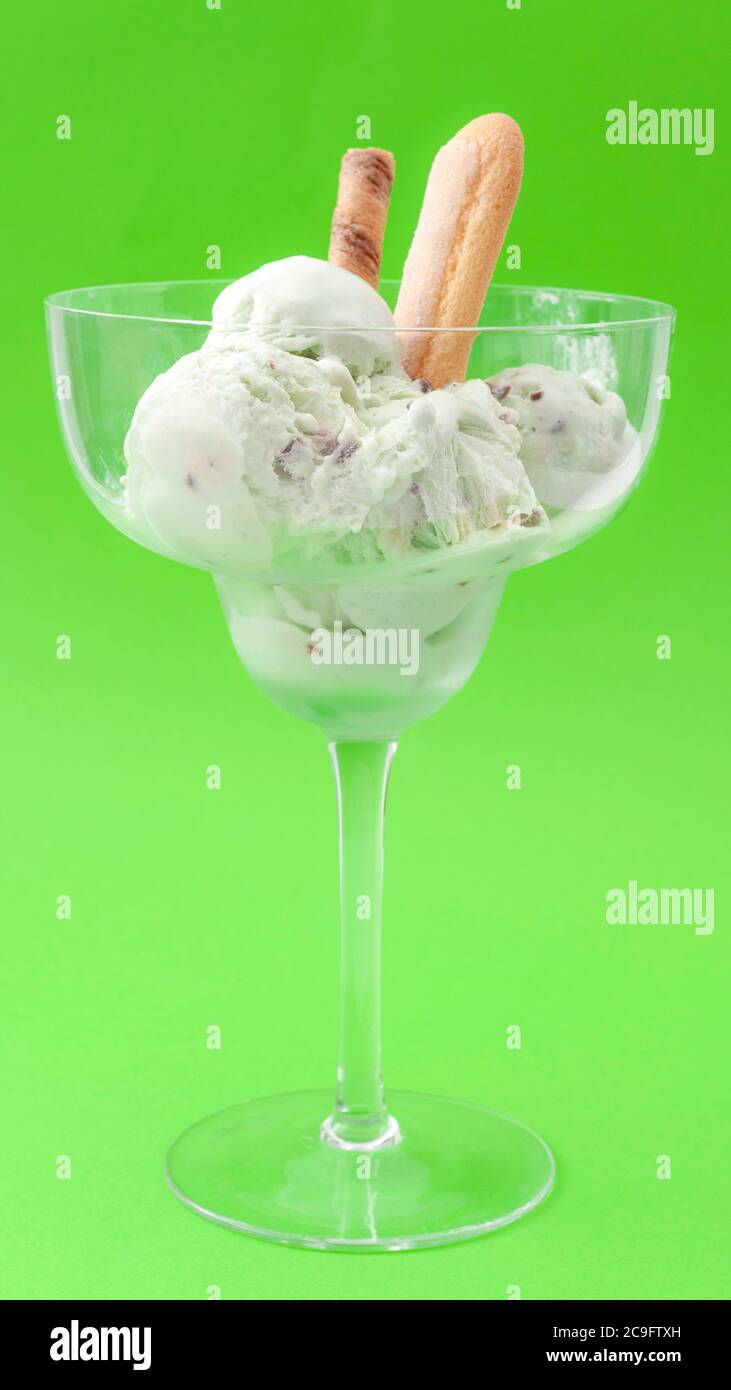 En-cas de produits laitiers congelés et concept de traitement rafraîchissant avec glace à la menthe fondue au goût de pistache dans un gobelet en verre isolé sur fond vert Banque D'Images