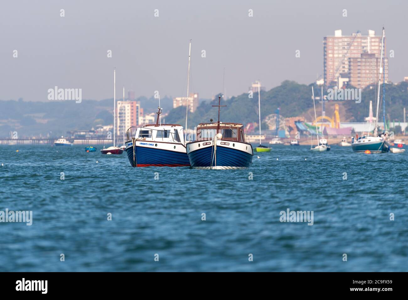 Deux bateaux bleus et blancs dans l'estuaire de la Tamise au large de Thorpe Bay, Southend on Sea, Essex, Royaume-Uni. Southend sur Sea Town Skyline. Artisanat de loisirs amarré dans l'eau Banque D'Images