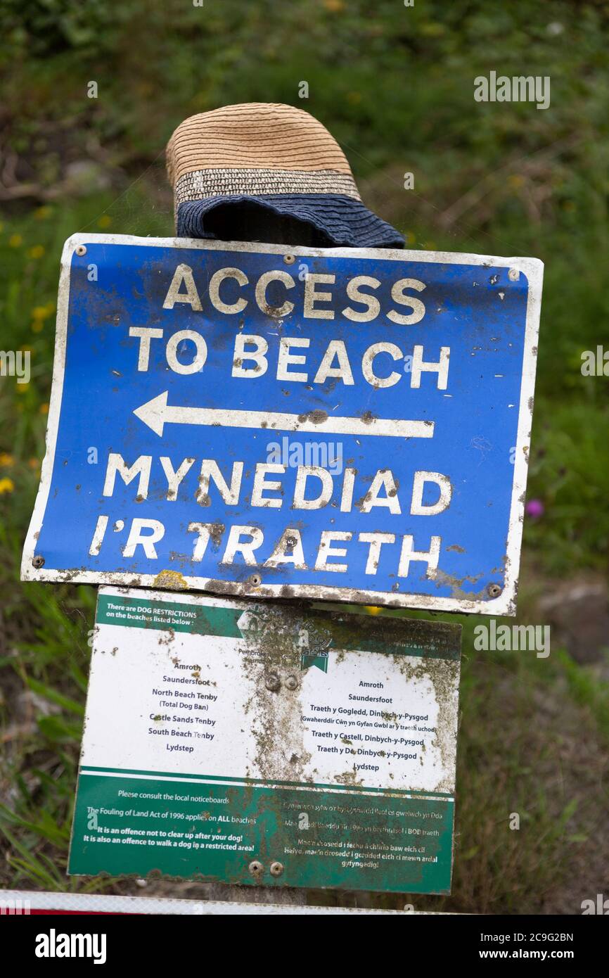Panneau bilingue en gallois et en anglais pointant vers l'entrée d'une plage au pays de Galles, avec chapeau de soleil placé sur le dessus. Banque D'Images