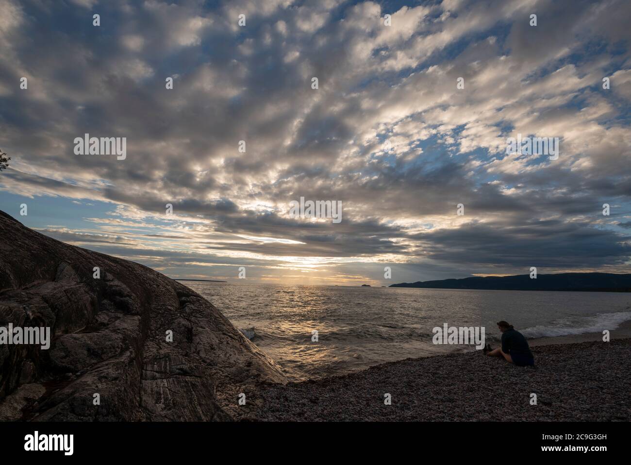 Une femme s'assoit sur la plage dans le parc provincial du lac supérieur pour observer le coucher du soleil. Banque D'Images