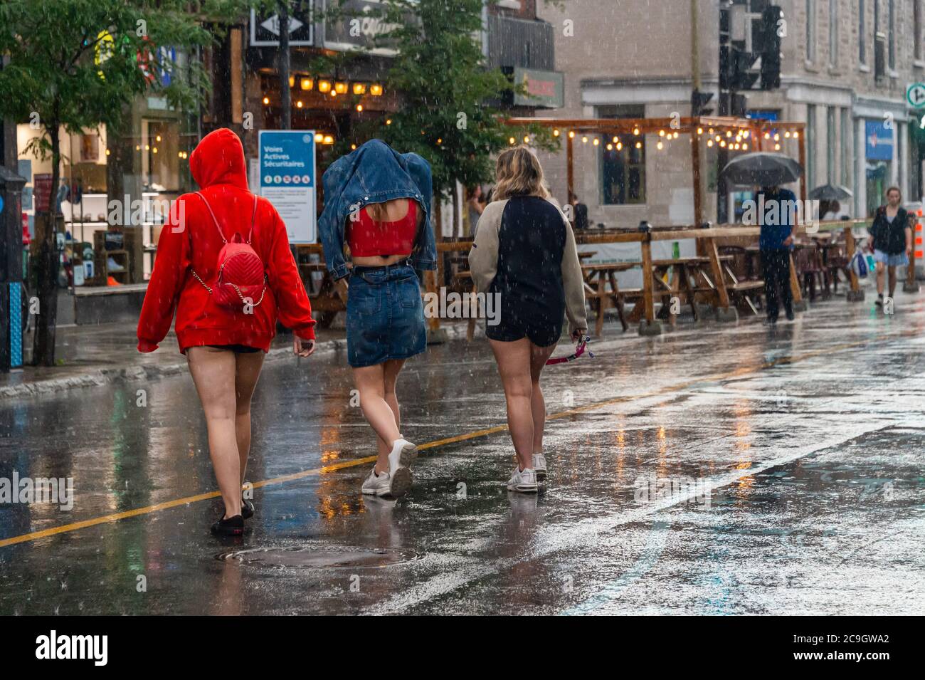 Montréal, CA - 30 juillet 2020 : trois jeunes femmes marchent sur l'avenue Mont-Royal sous la pluie et la tempête Banque D'Images