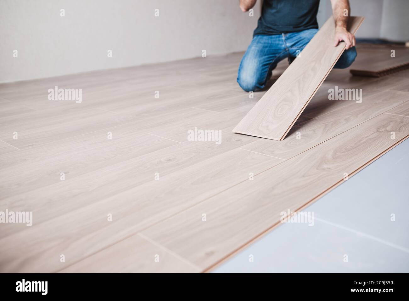 Homme en Jean sur un nouveau plancher stratifié - décor de plancher de bois - maître de pose stratifié Banque D'Images