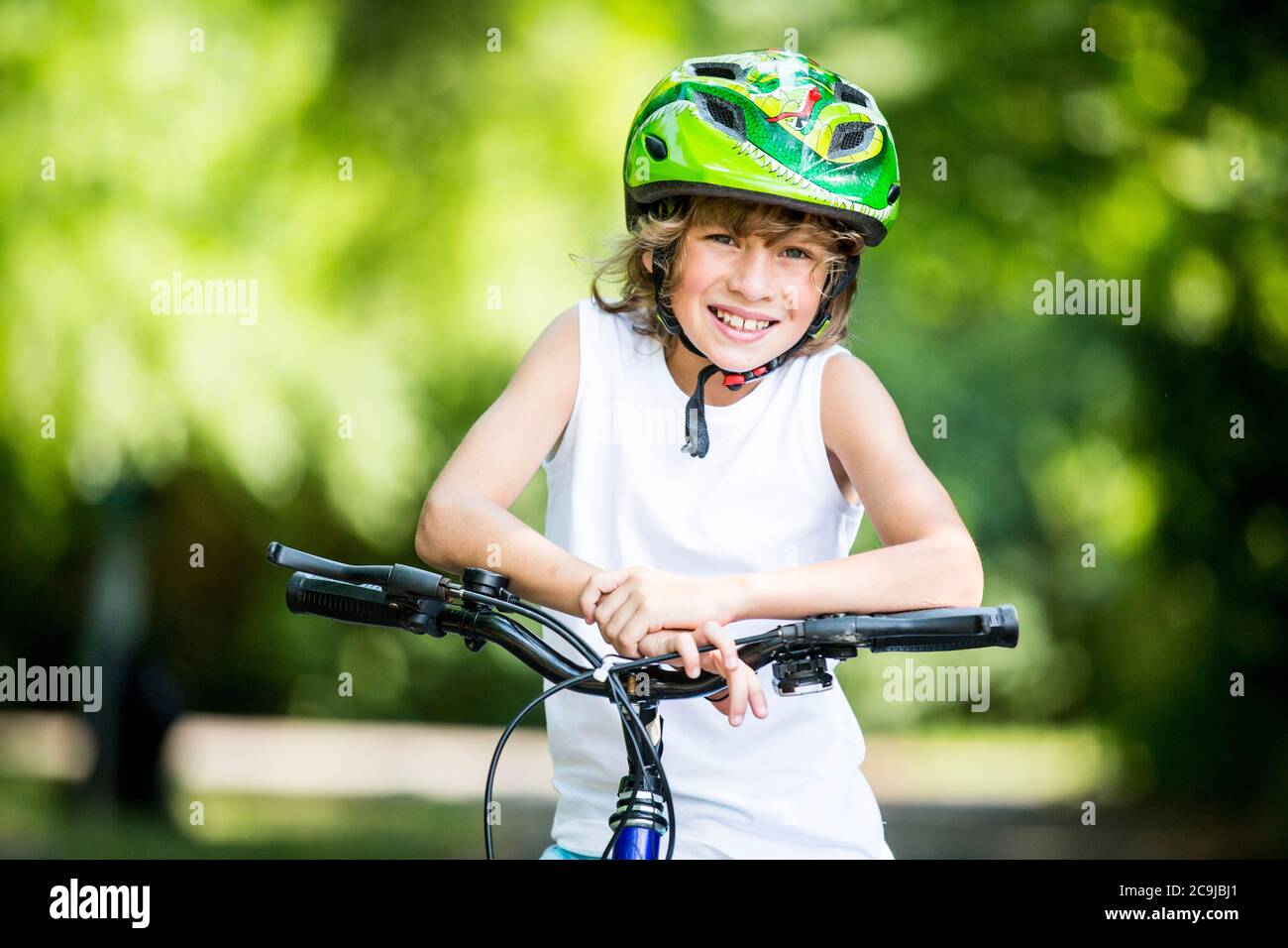 Garçon portant un casque de vélo et assis sur un vélo dans le parc, souriant, portrait. Banque D'Images