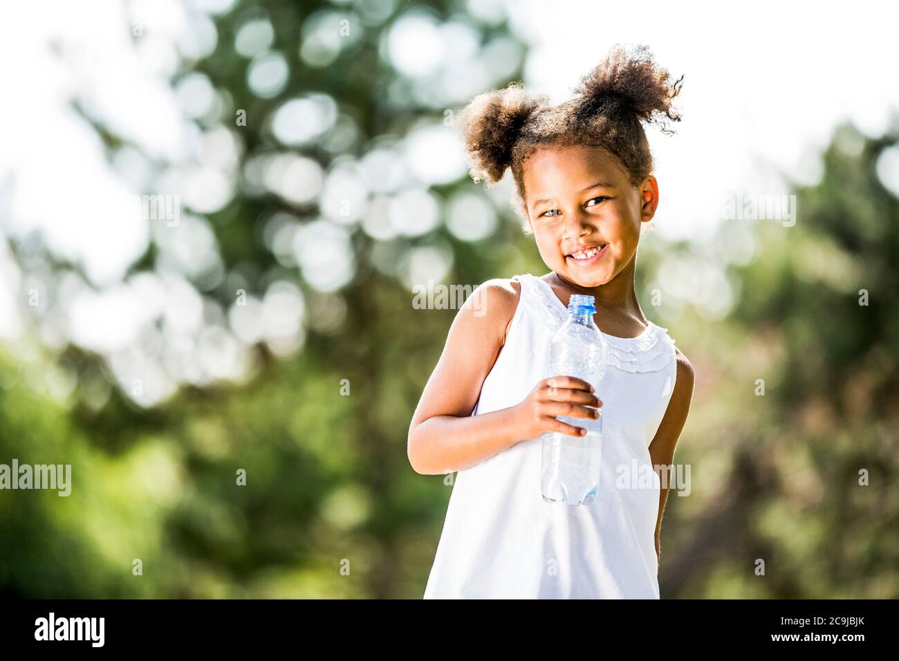 Fille debout avec une bouteille d'eau dans le parc, souriante, portrait. Banque D'Images