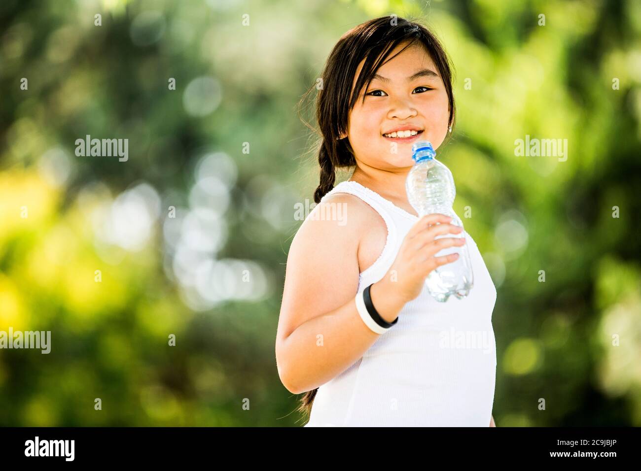 Fille debout avec une bouteille d'eau dans le parc, souriante, portrait. Banque D'Images