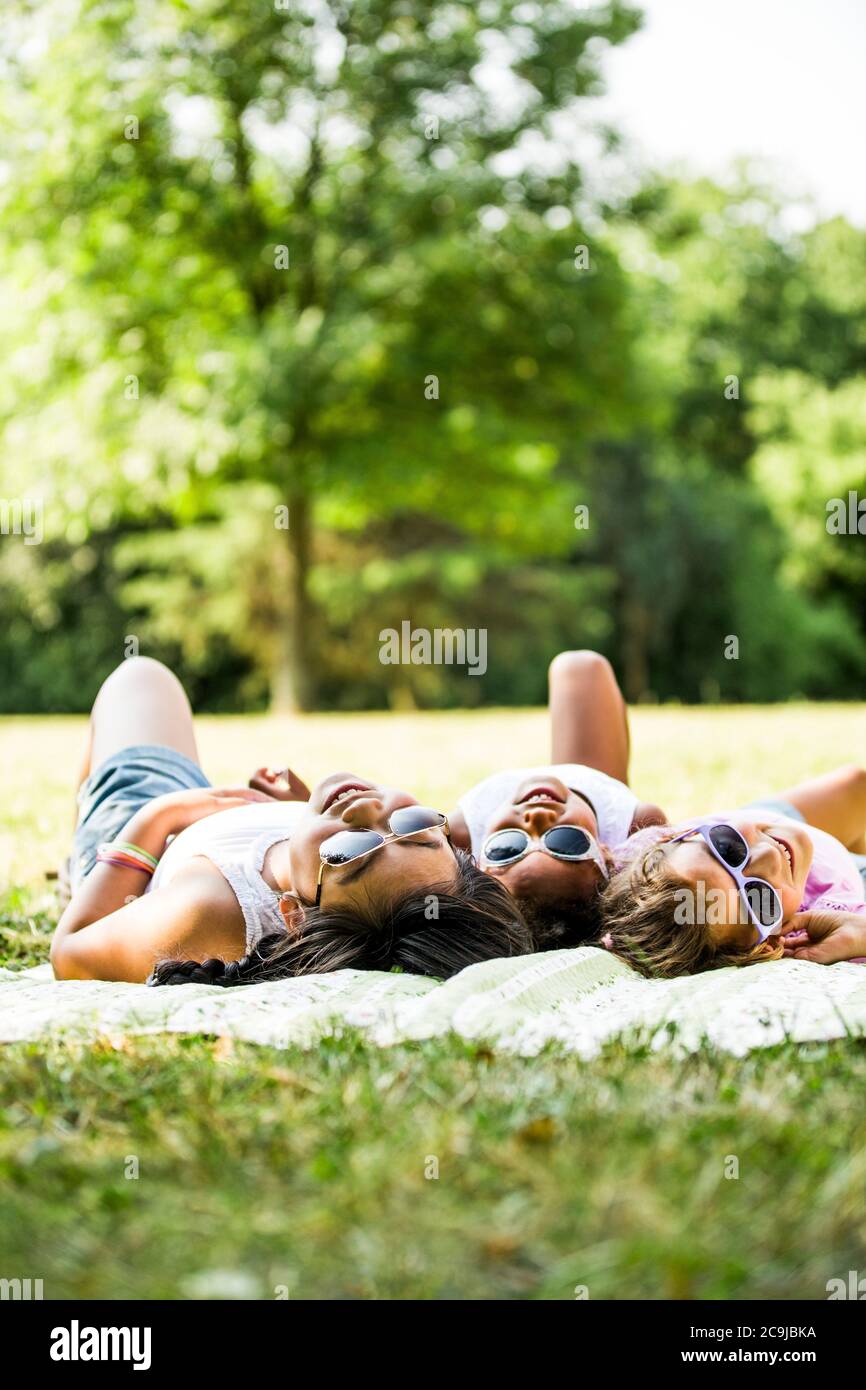 Filles portant des lunettes de soleil et couchée côte à côte sur une couverture dans le parc. Banque D'Images