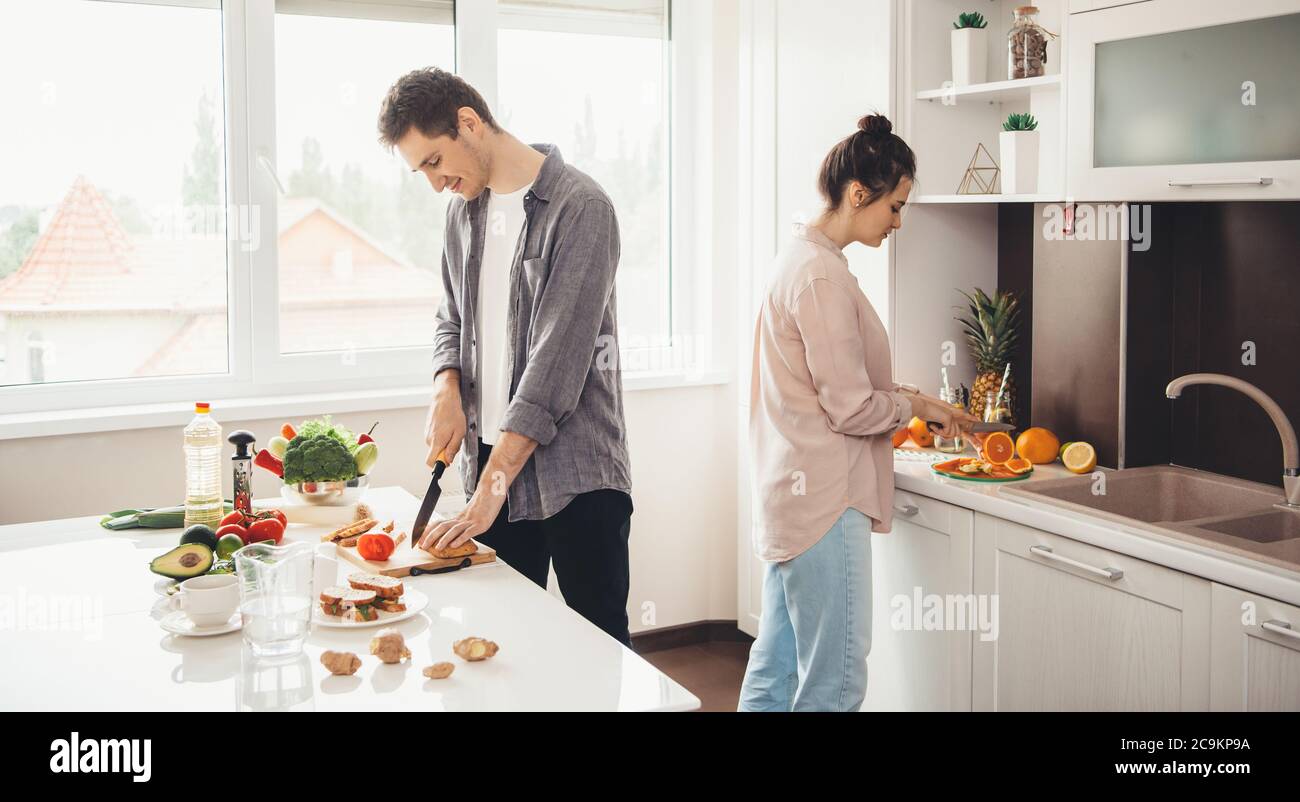 Un jeune couple caucasien coupe des fruits dans la cuisine et prépare le petit déjeuner ensemble Banque D'Images