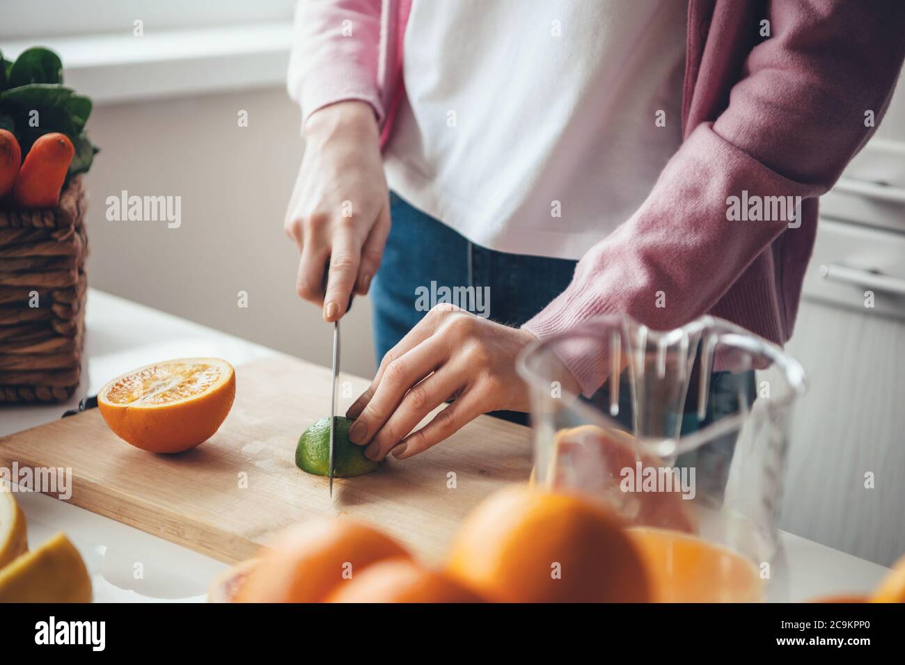 Gros plan d'une femme du caucase avec des cheveux rouges et des taches de rousseur en coupant un citron vert et une orange tout en faisant du jus frais à la maison Banque D'Images