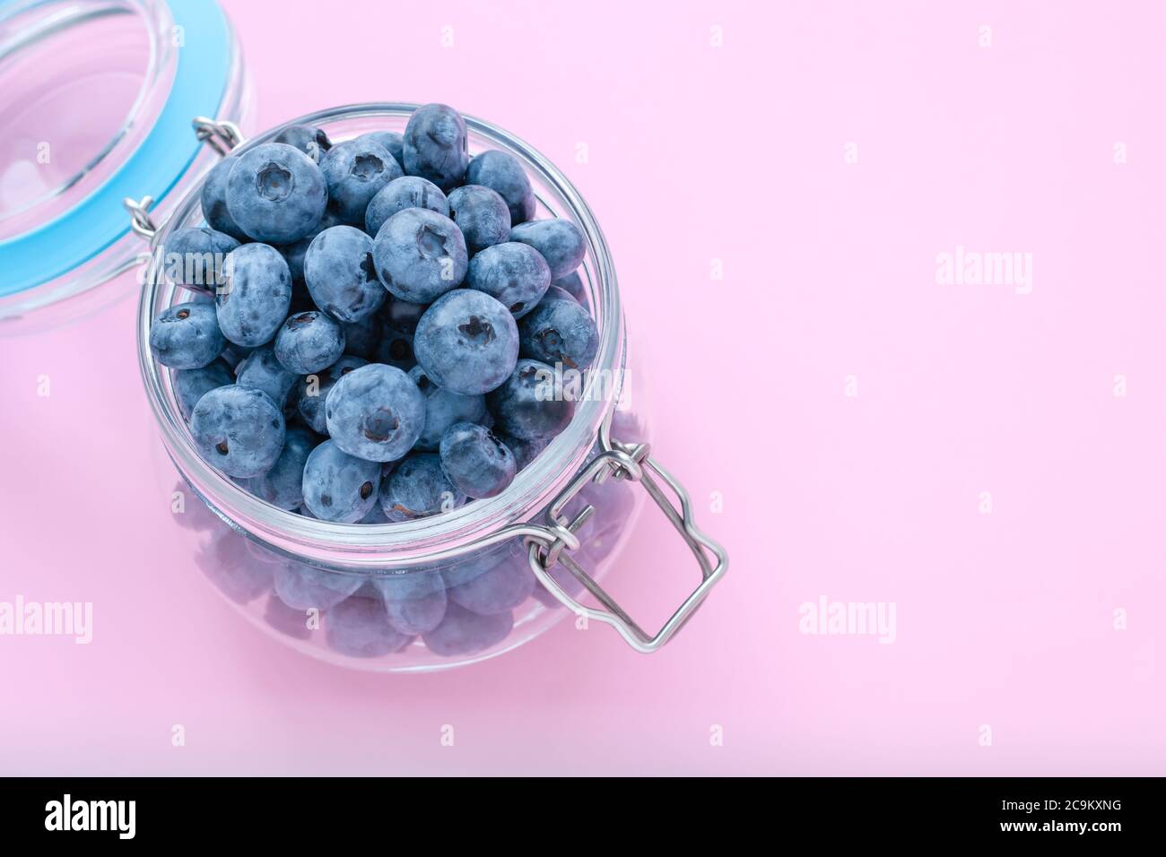 Bleuets dans un bol en verre ouvert sur fond rose, vue du dessus. Espace de copie, espace vide pour le texte. Une baie dans une verseuse en verre. Concept de cuisine végétarienne Banque D'Images