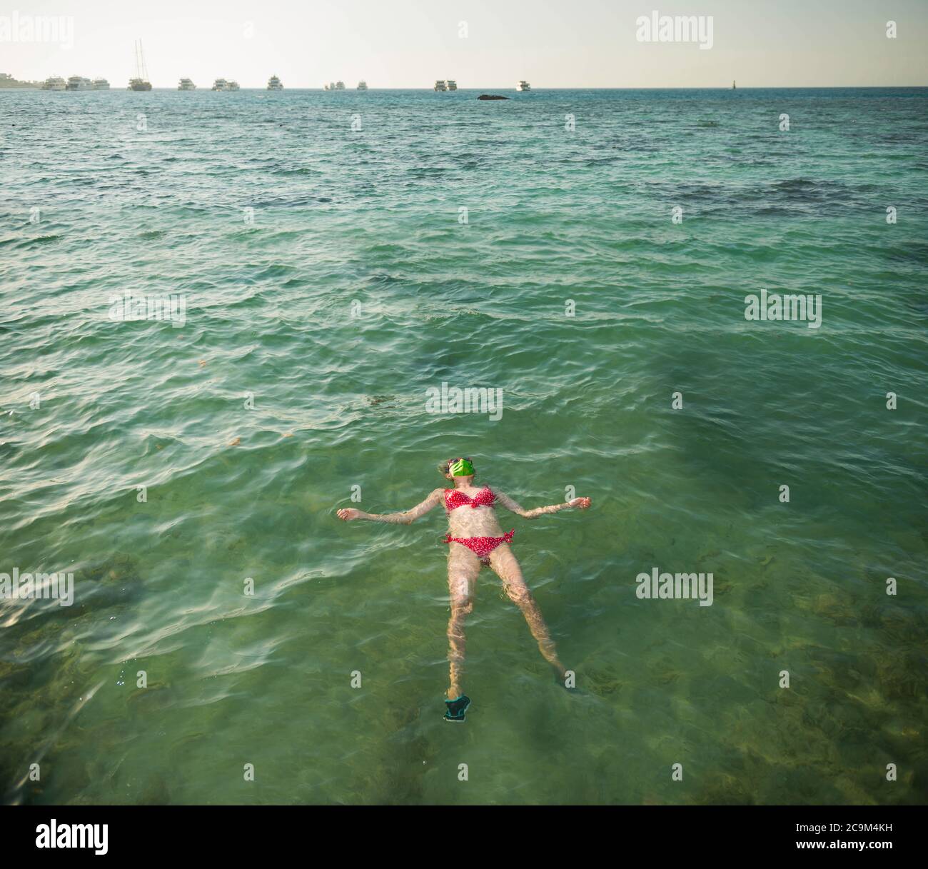 femme touristique en costume de bain rouge et masque vert sur l'eau de mer avec des bateaux à l'horizon Banque D'Images