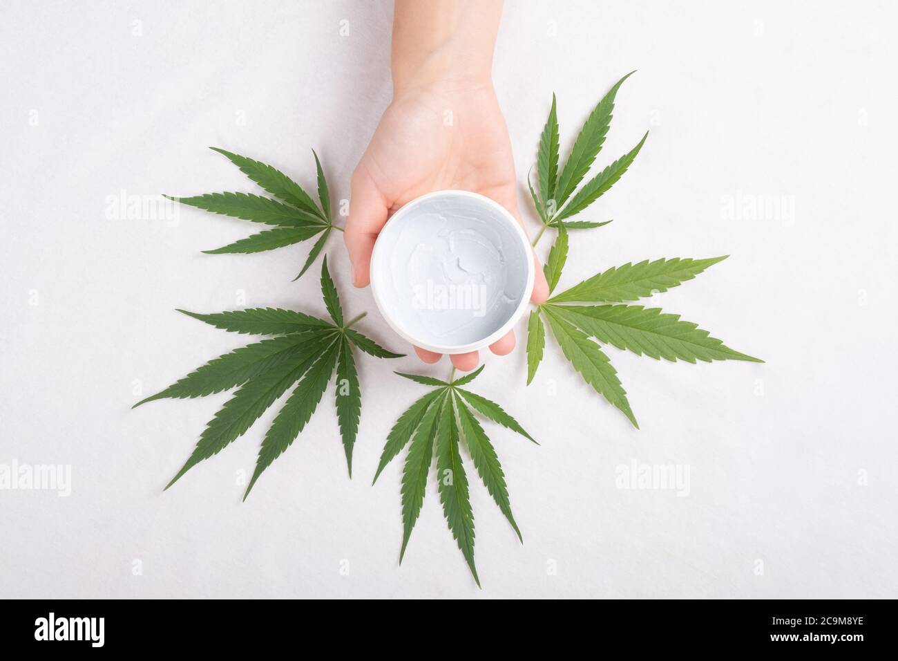 Gommage nettoyant dans la paume avec la feuille de plante de marijuana isolée sur fond blanc. Beauté, soins de la peau cosmétiques. Banque D'Images