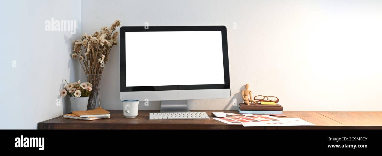 Un espace de travail en bois est entouré d'un moniteur d'ordinateur blanc à écran blanc et de divers équipements. Banque D'Images