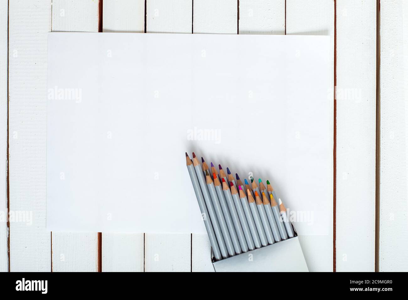 plusieurs crayons de couleur qui regardent d'un paquet qui sont sur la feuille de papier couché sur une table en bois de tableau blanc. Banque D'Images