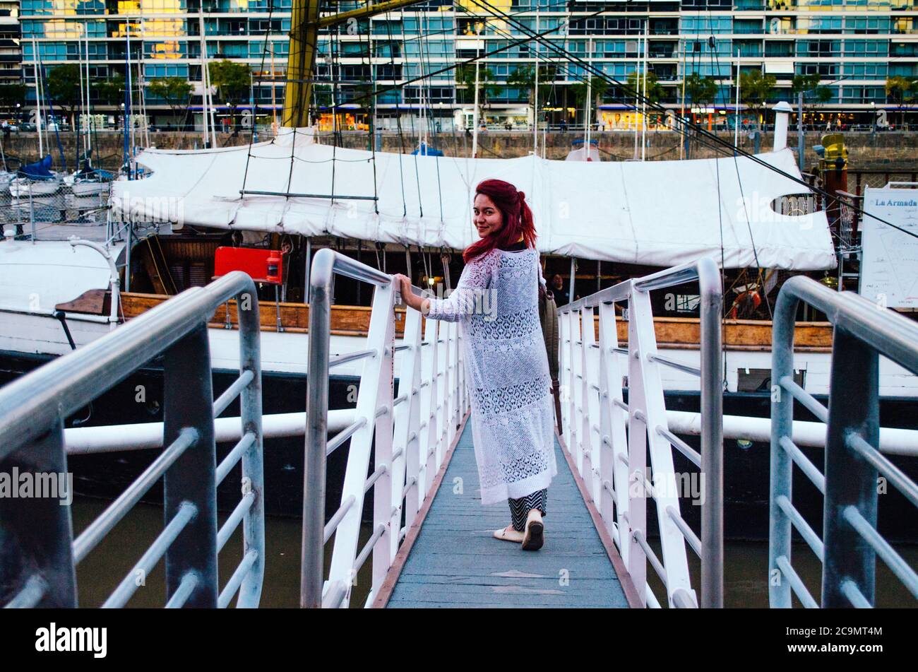 Une femme brésilienne à tête rouge dans ses années 20s entrant dans un grand bateau garée dans le quartier des affaires de Puerto Madero et regardant de nouveau à la caméra et souriant. Banque D'Images