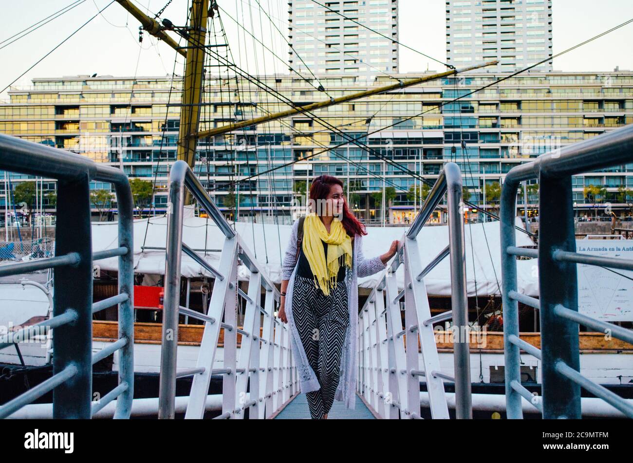 Une femme brésilienne à tête rouge dans ses années 20s entrant dans un grand bateau garée dans le quartier des affaires de Puerto Madero et regardant à côté et souriant. Banque D'Images