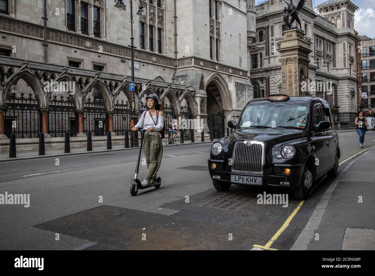 Femme voyageant le long de la route sur Fleet Street sur un scooter électrique passé un taxi noir de Londres, City of London, Royaume-Uni Banque D'Images