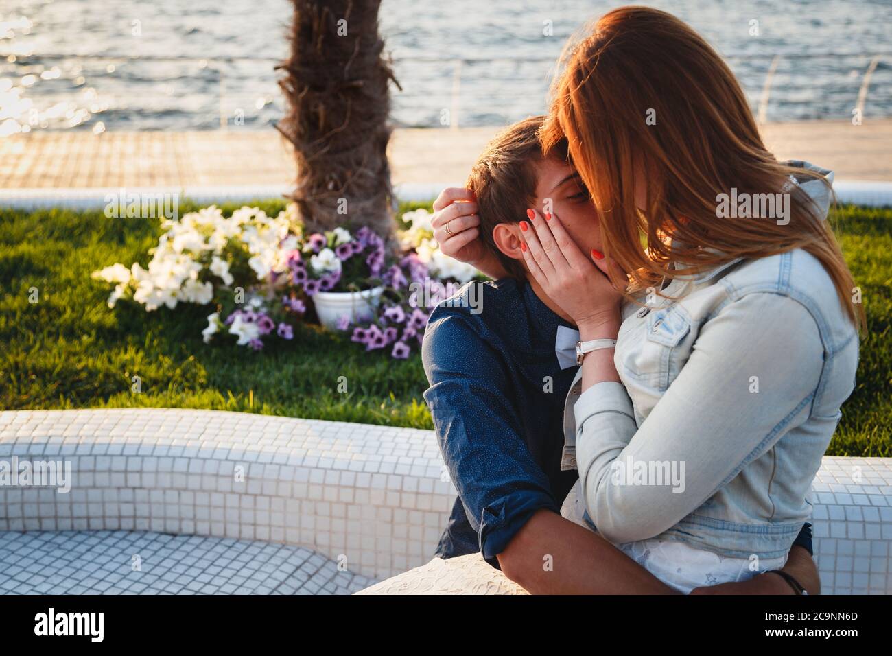 Mignon jeune beau couple assis et s'embrassant ensemble au bord de la mer Banque D'Images
