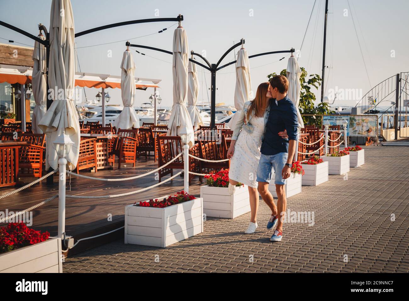 ODESSA, UKRAINE - 06 AOÛT 2015: Joli jeune beau couple embrassant à la jetée au port avec de petits yachts et café d'été, heureux sourire en plein air Banque D'Images