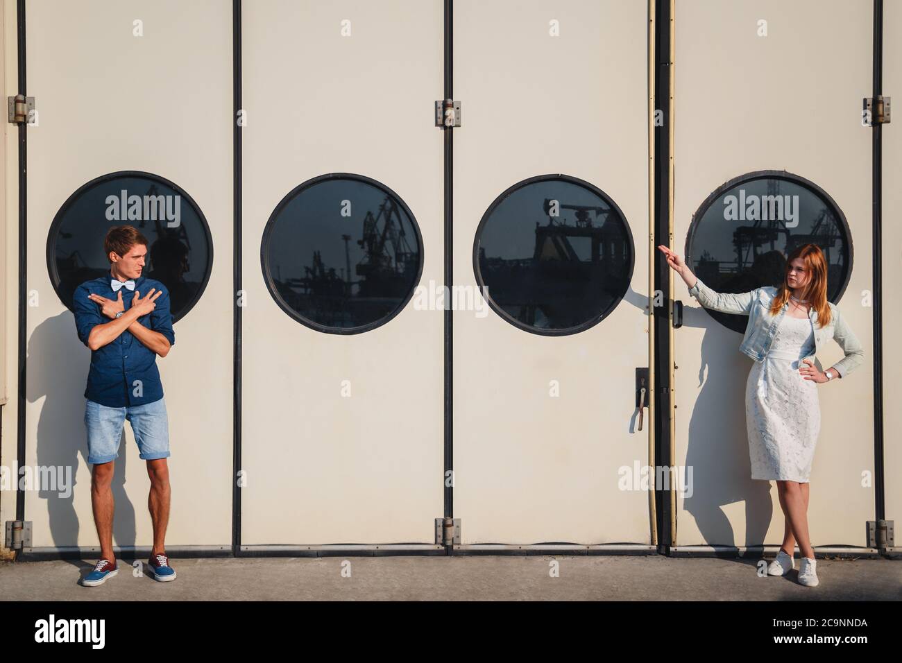 Mignon jeune beau couple de taille basse au port, sur le mur blanc avec de grands hublots arrière-plan, heureux sourire portrait d'extérieur Banque D'Images