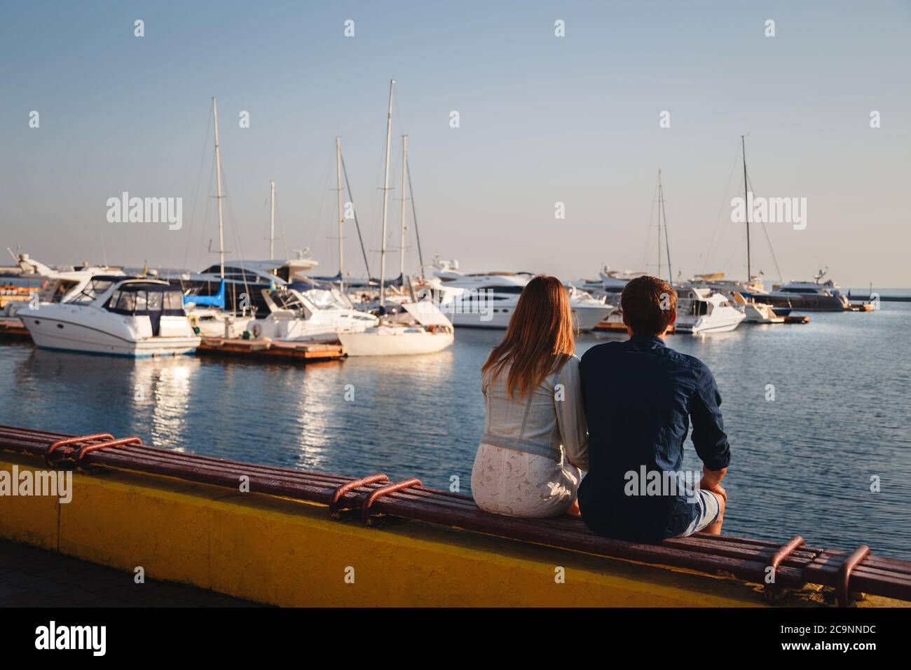 Mignon jeune beau couple assis et s'embrassant ensemble à la jetée au port, des hipsters. Vue arrière Banque D'Images