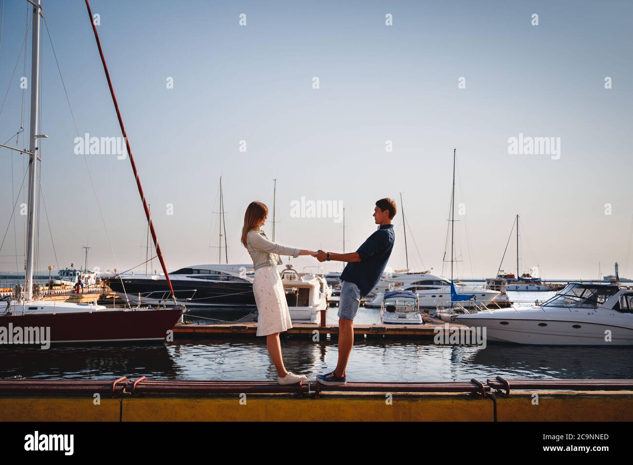 Mignon jeune beau couple à la jetée au port avec de petits yachts, hipster, heureux sourire portrait extérieur Banque D'Images