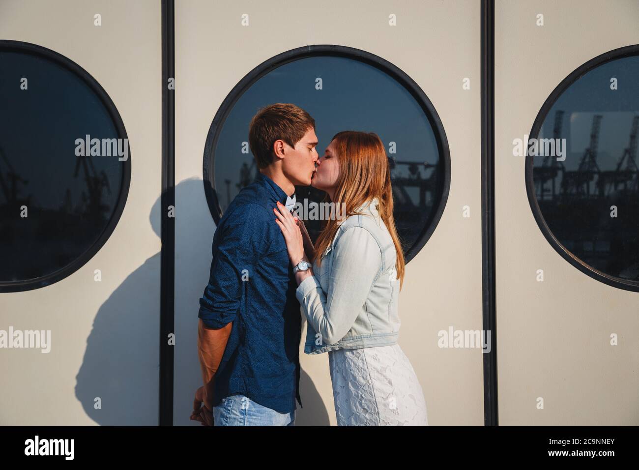 Mignon jeune beau couple hipster embrassant au port, sur le mur blanc avec de grands hublots arrière-plan Banque D'Images
