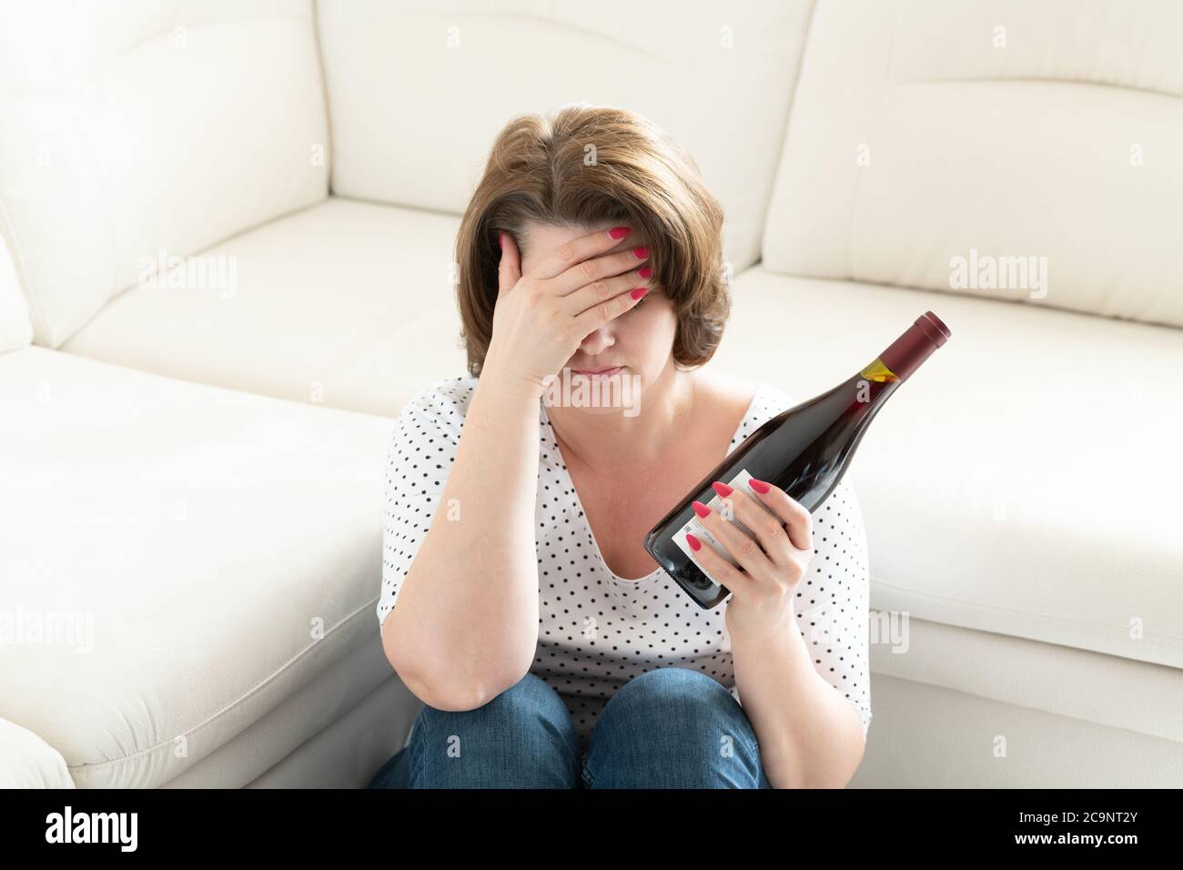Femme avec un mal de tête et une bouteille de vin. Gueule de bois Banque D'Images