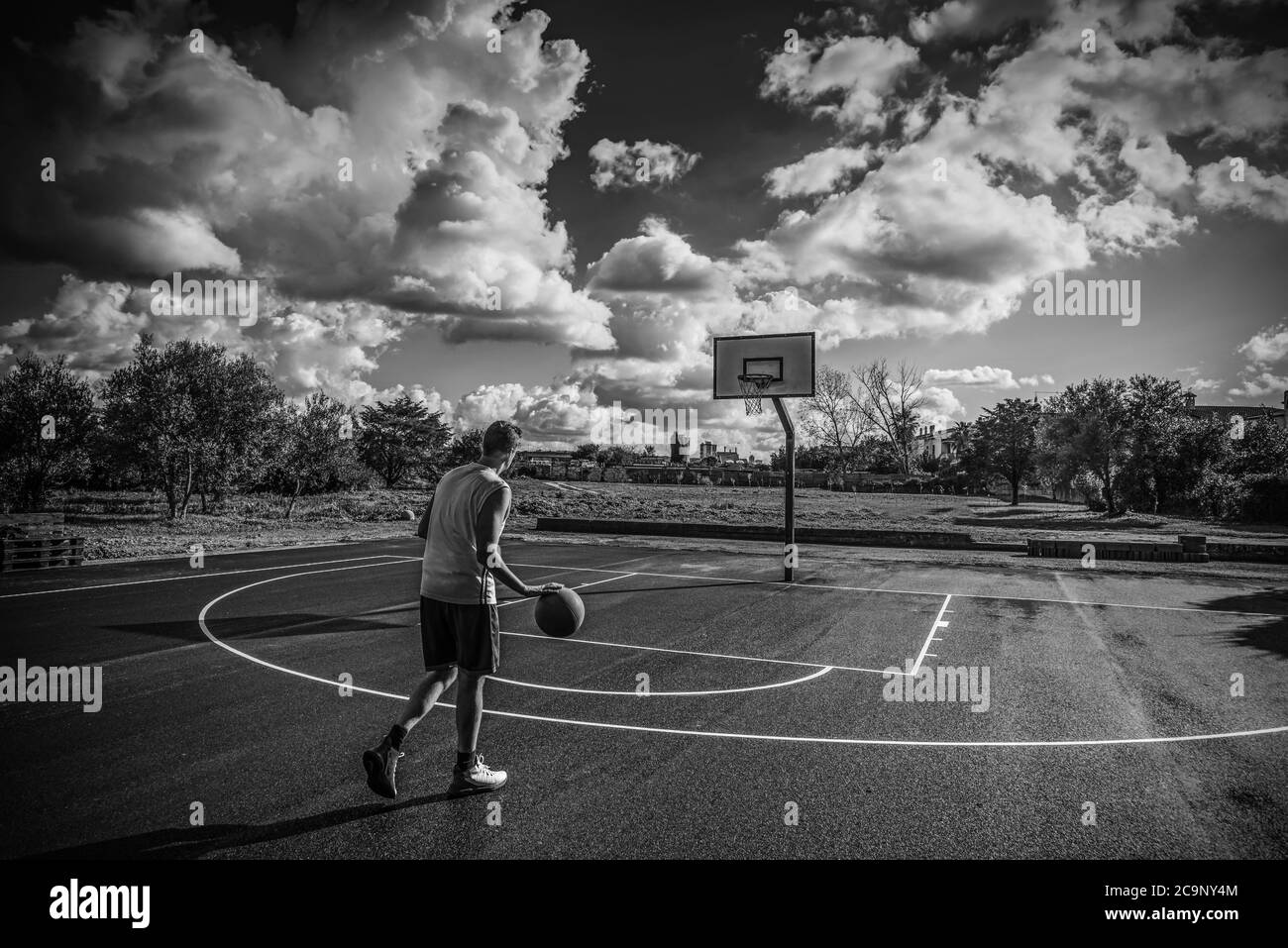 Un joueur de basket-ball s'est enfuillé dans un terrain de jeu par une journée nuageux. Effet noir et blanc Banque D'Images